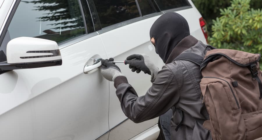 Thief attempting to break into a white car in a residential area